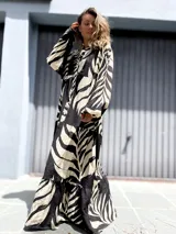 Vestido largo de manga larga, con cuello camisero y estampado de hojas tropicales en blanco y negro. El diseño presenta un corte amplio con volados en la falda.