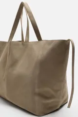Bolso tipo shopper color topo, fabricado en piel con acabado serraje. Cuenta con dos asas de mano y un bolsillo pequeño con cierre mediante cremallera en su interior.
