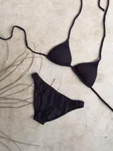 Conjunto de bikini verde esmeralda con textura acanalada. El corpiño es de triángulos movibles con tiras finas para atar al cuello y a la espalda, y tiene almohadillas desmontables. La bombacha es vedetina ancha con laterales fijos.
