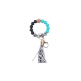 Llavero pulsera con cuentas de silicona en color turquesa, negro y animal print, con dije de flecos en cuero sintético color gris claro y herrajes dorados.