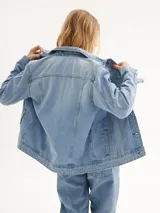 Chaqueta de jean celeste de corte clásico, con cuello tipo camisa, cierre frontal con botones, bolsillos delanteros con solapa y mangas largas con puños abotonados.