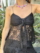 Top negro de encaje con breteles finos, detalle fruncido en el escote y abertura frontal cubierta por un nudo.