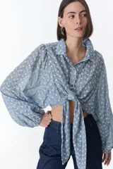 Camisa celeste con estampado de flores blancas, corte cropped, cuello camisero, mangas largas abullonadas con puños elásticos y cierre frontal con botones.