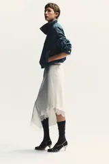 Chaqueta corta de denim azul con cuello alto, manga larga con hombros caídos, bolsillos laterales, bajo con elástico y cierre frontal con cremallera y botones ocultos.