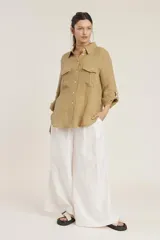Camisa de lino color beige con cuello clásico, cierre frontal con botones, mangas largas con trabillas para enrollar y dos bolsillos con solapa en el pecho.