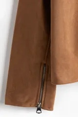 Campera de gamuza color camel, con cuello camisero, cierre frontal y bolsillos laterales con cierre. Presenta un corte estándar y forro interior.