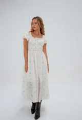 Vestido corto color crema con estampado floral, escote cuadrado con lazo ajustable, mangas cortas abullonadas y corte princesa.