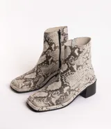 Bota corta de cuero charol negro, con caña baja, cierre lateral y taco cuadrado de madera.