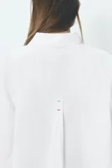 Camisa blanca oversize de popelina de algodón, con cuello solapa, manga larga con puños y cierre frontal con botones ocultos. Detalle de hilo de contraste en los botones.