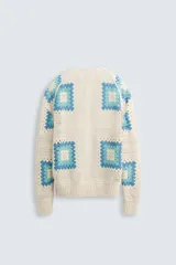 Cárdigan de punto color crudo con diseño de cuadrados de crochet en tonos celeste y azul. Tiene cuello en V, manga larga, bolsillos frontales y cierre con botones.