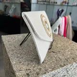 Sobre de fiesta color crudo, tejido artesanalmente en la India. Tiene aplique central bordado con mostacillas, cristal e hilo en tonos dorados y crudo. Incluye asa de cadena dorada para colgar del hombro.