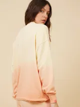 Sweater color crema con degradé a naranja, con cuello redondo y logo estampado de palmera en el pecho.