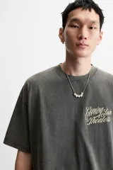 Camiseta gris oscuro con efecto lavado, cuello redondo y manga corta. Tiene un bolsillo en el pecho y estampados en el frente y la espalda.