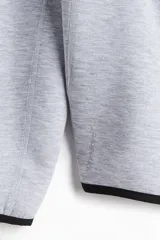 Campera deportiva gris con capucha, cierre frontal y bolsillos laterales con cierre. Confeccionada en tejido funcional DryMove™ que ayuda a absorber el sudor.
