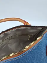 Cartera tipo bowling de jeans azul con detalles en cuero sintético color camel. Incluye llavero de peluche y dije de flor.