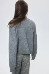 Cárdigan de punto gris jaspeado, con cuello en V, botones frontales y dos bolsillos delanteros abiertos. Presenta un corte holgado y hombros caídos, con puños y bajo acanalados.