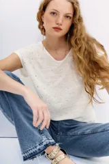 Remera de lino color crudo con cuello en V y mangas cortas. Tiene tachas plateadas termofijadas en el frente.