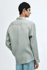 Camisa de lino color gris con cuello inglés, tapeta clásica, canesú en la espalda, mangas largas con tapeta de manga y botón, cierre ajustable de botón en los puños y bajo redondeado.
