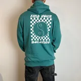 Canguro verde con capucha y cordones ajustables, con estampado en la espalda de un símbolo de yin y yang dentro de un cuadrado con diseño de tablero de ajedrez, y las frases "Find Your" en la parte superior y "Balance" en la parte inferior.