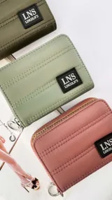 Billetera corta con cierre alrededor y tapa, confeccionada en tela capitoneada. Incluye varias reparticiones con tarjeteros y bolsillos internos, y una correa de mano desmontable. Disponible en negro, rojo y dorado.