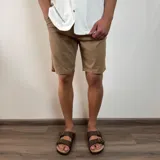 Bermuda color beige claro, estilo chino, confeccionada en gabardina. Presenta un corte recto y dobladillo en el ruedo.