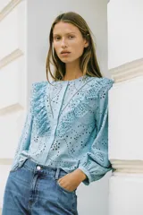 Camisa celeste de cuello redondo y manga larga, con bordados perforados y volantes. Cierre frontal con botones ocultos por solapa.