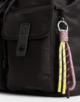 Mochila de tela color lila, con solapa con broche y tira de ajuste, doble bolsillo frontal con broche y pouch con charm lateral en forma de cartera.