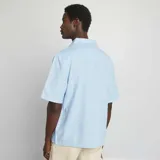 Camisa celeste de lino con corte regular, cuello clásico y manga corta.
