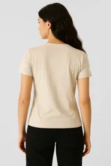 Remera color beige con cuello redondo y mangas cortas. Presenta apliques bordados con motivos geométricos y borlas en el frente.