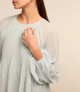 Blusa celeste de crepé con textura plisada, cuello redondo, mangas largas abullonadas y puños ajustados.