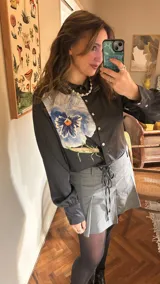 Camisa crop negra con estampado de una flor y un insecto, con cintas para atar en la cintura.