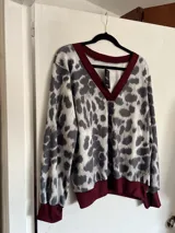 Sweater de punto con cuello en V y estampado animal print en tonos grises y blancos. Tiene ribete marrón en el cuello, puños y bajo elastizados.