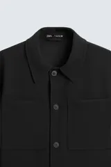 Sobrecamisa negra de corte cuadrado, con cuello solapa, manga larga con puños abotonados, bolsillos tipo parche en el pecho, bolsillos laterales y cierre frontal con botones.