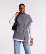 Poncho de punto color gris con cuello alto y diseño de manga corta sin sisa. Incluye un cinturón del mismo material para ajustar a la cintura y presenta una textura acanelada.