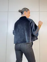 Chaqueta corta negra de terciopelo con cuello alto, manga corta y cierre frontal con botones grandes.