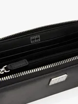 Billetera Tommy Jeans negra con cierre de cremallera y logo plateado en el frente. Incluye múltiples ranuras interiores para tarjetas, tres compartimentos principales, dos compartimentos interiores para billetes y un bolsillo interior con cremallera.