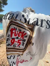 Remera marrón con estampado de un reloj dorado y la frase "Who wears a watch in Ibiza?".
