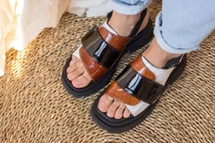 Sandalias marrones con tiras anchas de cuero texturizado y gamuza, suela track negra y hebilla ajustable en el tobillo.