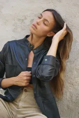 Camisa negra de cuero ovino con cuello mao, cierre frontal con botones a presión, dos bolsillos de parche en el pecho y tachas doradas en cuello, bolsillos y mangas.