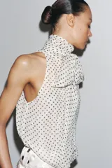 Top blanco con estampado de lunares negros, cuello halter con pañuelo y cierre con botón en la espalda.