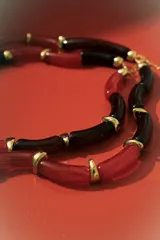 Collar de dos vueltas con eslabones tubulares curvos, alternando colores negro y rojo translúcido, separados por pequeños detalles metálicos dorados.