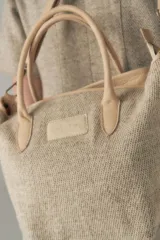 Cartera tipo tote de lana color beige con forro, cierre y asa de cuero regulable.