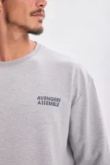 Buzo deportivo gris con cuello redondo y mangas largas. Estampado frontal con el texto "Avengers Assemble" en azul.