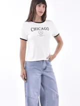 Remera negra de manga corta con cuello redondo y ribete blanco. Presenta un estampado frontal con el texto "CHICAGO" en blanco, un logo circular con una "M" en el centro y el texto "CULTURAL WIND CITY SINCE 2023" debajo.