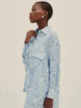 Camisa celeste y blanca con estampado de cebra, de corte holgado, con cuello clásico, cierre frontal con botones, mangas largas con puños abotonados y dos bolsillos de parche en el pecho.