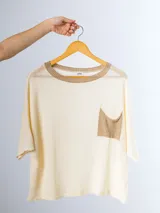Remera tejida en hilo italiano, color beige, con cuello a la base y bolsillo frontal. De caída relajada y silueta amplia.