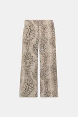 Pantalón de tiro alto con estampado de piel de serpiente en tonos beige y marrón. Tiene bolsillos laterales ocultos en la costura y falsos bolsillos de vivo en la espalda. El cierre frontal es con cremallera y ganchos metálicos.