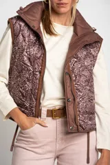 Chaleco marrón acolchado con cuello alto, cierre frontal con broches a presión y dos bolsillos delanteros con cordón ajustable.