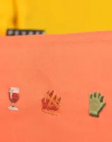 Neceser naranja de tela con cierre superior y logo de la marca en etiqueta negra. Presenta bordados de emojis: copa de vino, fuegos artificiales y mano verde.