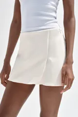 Falda pantalón corta color blanco, de tiro medio con abertura en el delantero y cierre lateral con cremallera.